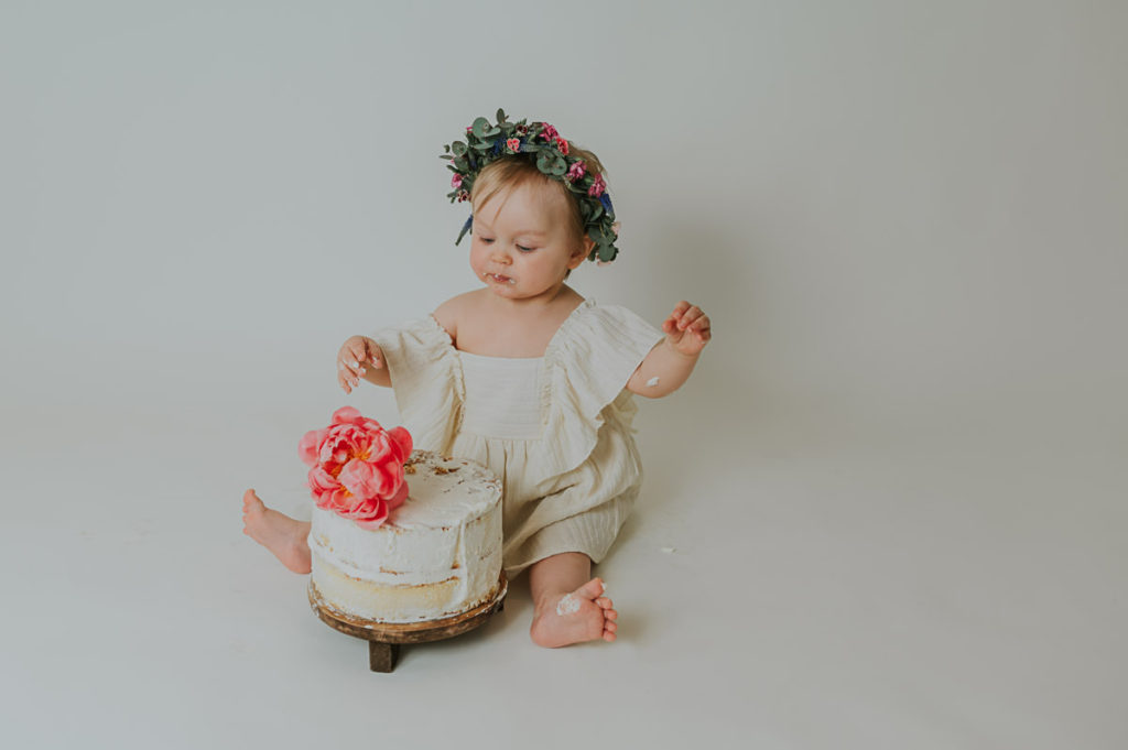 Ettårsfotografering cake smash for en baby jente - babyen smaker på kaken sin og har en nydelig blomsterkrans på hodet. Fotografering er i Alta i fotostudio TS Foto Design