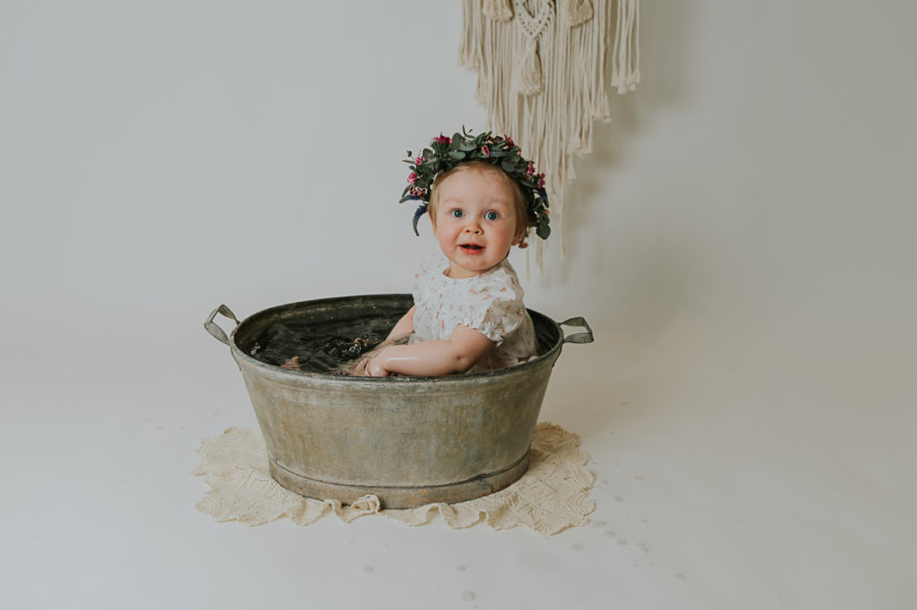 Ettårsfotografering i fotostudio i Alta TS Foto Design. Babyen sitter i en sinkbalje med en fin blomsterkrans på hodet. 