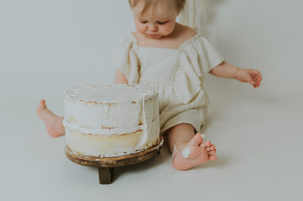 Ettårsfotografering cake smash for en baby jente - babyen smaker på kaken sin - det er masse krem på foten hennes