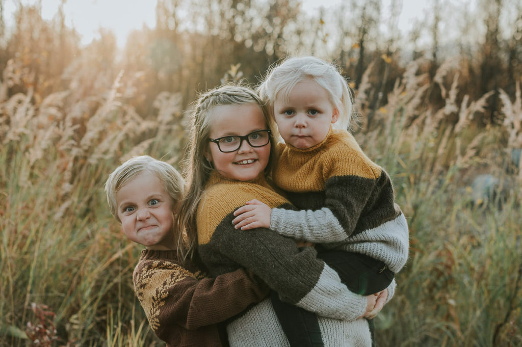 Søskenfotografering i Alta om høsten. Tre barn har på seg hjemmestrikkede genser i varme høstfarger
