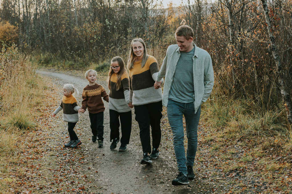 Familiefotografering i Alta om høsten - familie på fem tar en tur i høstskog  blant nydelige høstfarger - alle holder hverandre i hendene og spaserer i skogen