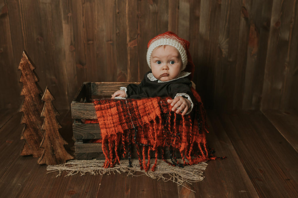 Julefoto med liten baby som sitter i en tre-eske med nisselua på 