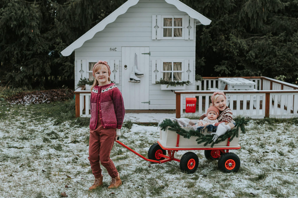 Julekortfotografering utendørs med en baby og storesøsken. Eldste søster triller en vogn med små søsken 