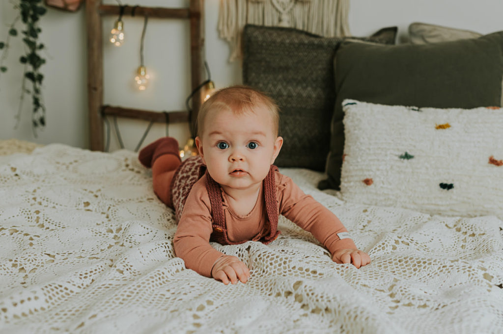 Lifestyle babyfotografering - utvikling fra måned til måned  - skjønn baby jente ligger på en storseng i boho stil 