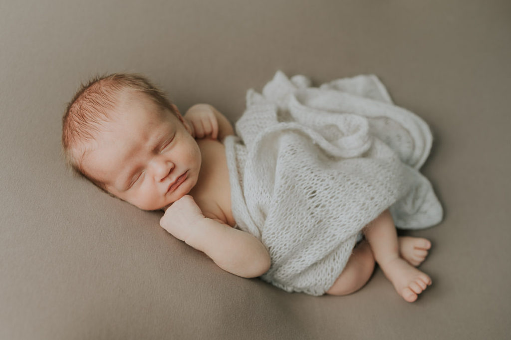 Cute baby boy sleeping on a beige photo backdrop during newborn photo session
