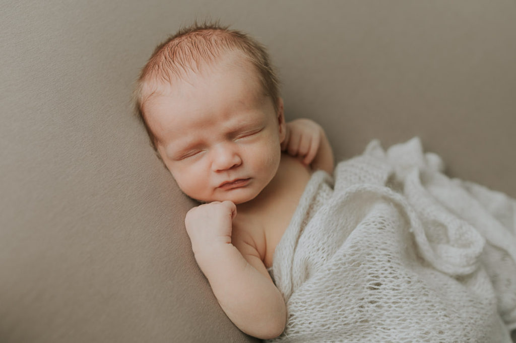 Cute baby boy sleeping on a beige photo backdrop during newborn photo session