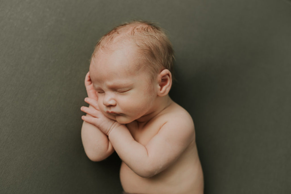 Cute baby boy sleeping on a dark green photo backdrop during a newborn session in Norway