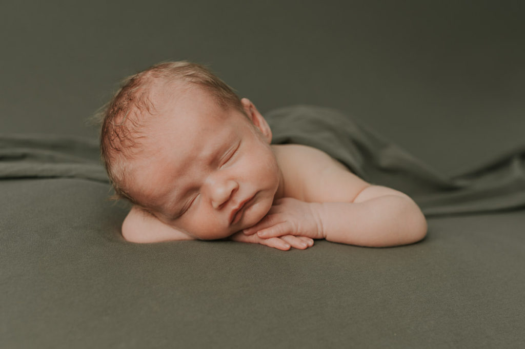 Cute baby boy sleeping on a dark green photo backdrop during a newborn session in Norway - pose chin on hands