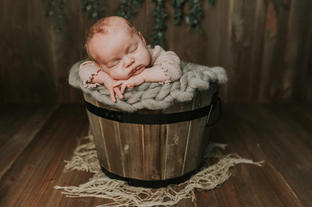 Nydelig nyfødt jente 1 måned gammel baby i en brun bøtte sover på nyfødtfotografering 