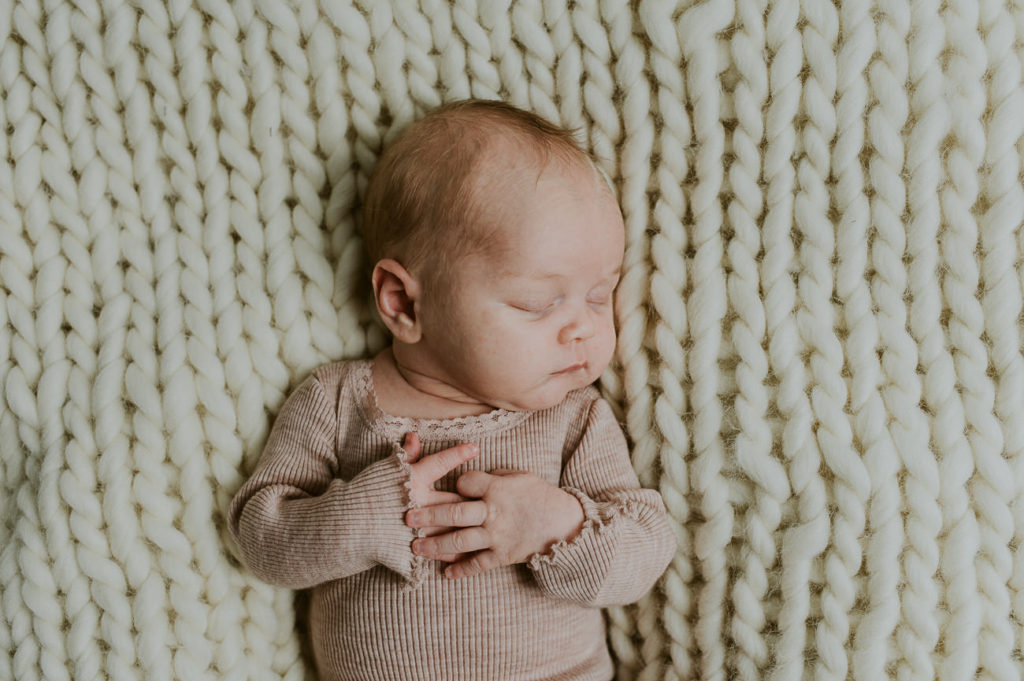 Nyfødt baby jente sover på en fingerstrikket  chunky wool teppe