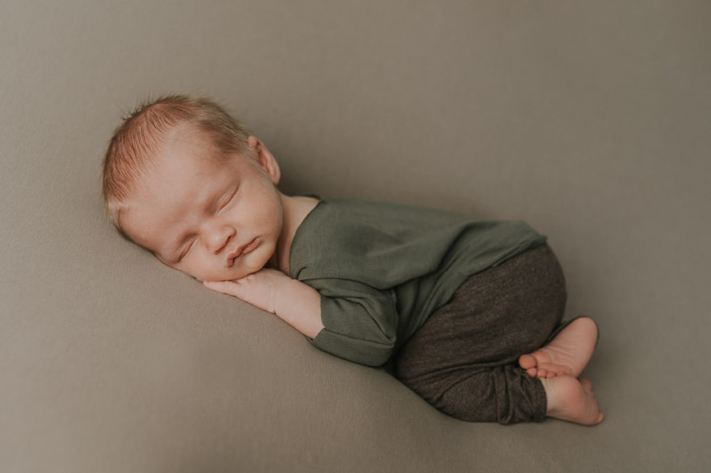 Beautiful newborn baby sleeping on his tummy on a beige backdrop in photo studio in Norway for his newborn session