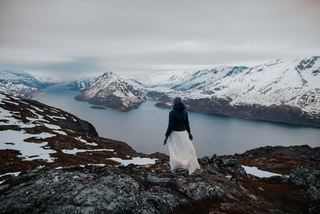 Bride standing on a mountaintop watching beautiful fjords near Alta in Norway - captured by Norway elopement photographer TS Foto Design