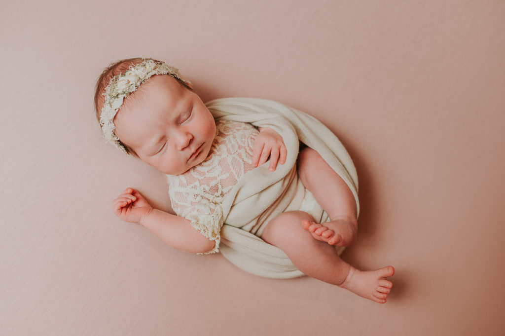 Baby jente med blonderbody og hårbånd på seg sover på nyfødtfotografering i Alta