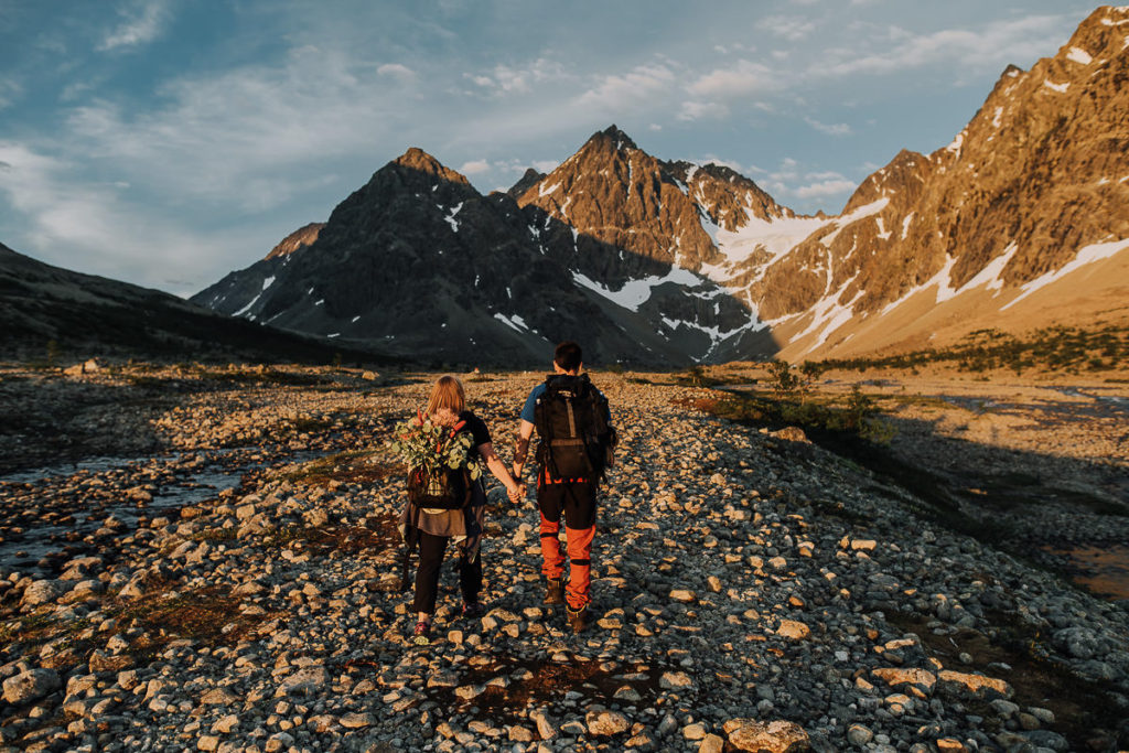 Bride and groom in hiking outfits facing beautiful mountains of Lyngen Alps