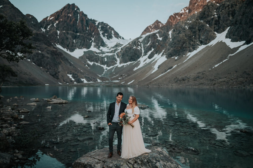 Bride and groom portrait in front of a blue glacial lake and mountains in Norway