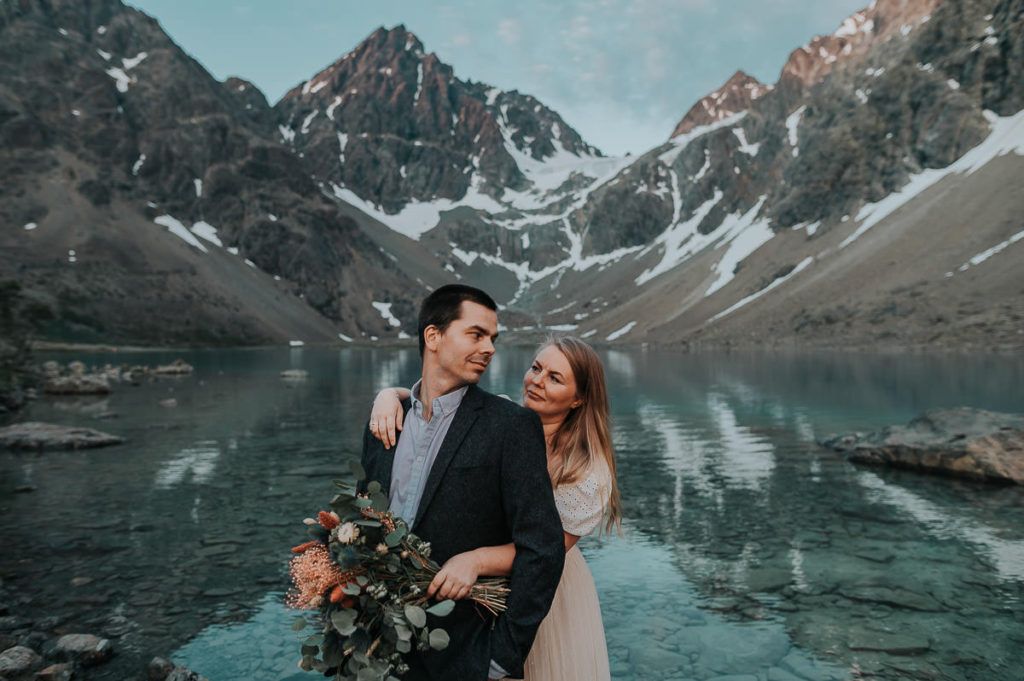Bride and groom hugging each other among beautiful mountains and lake landscape