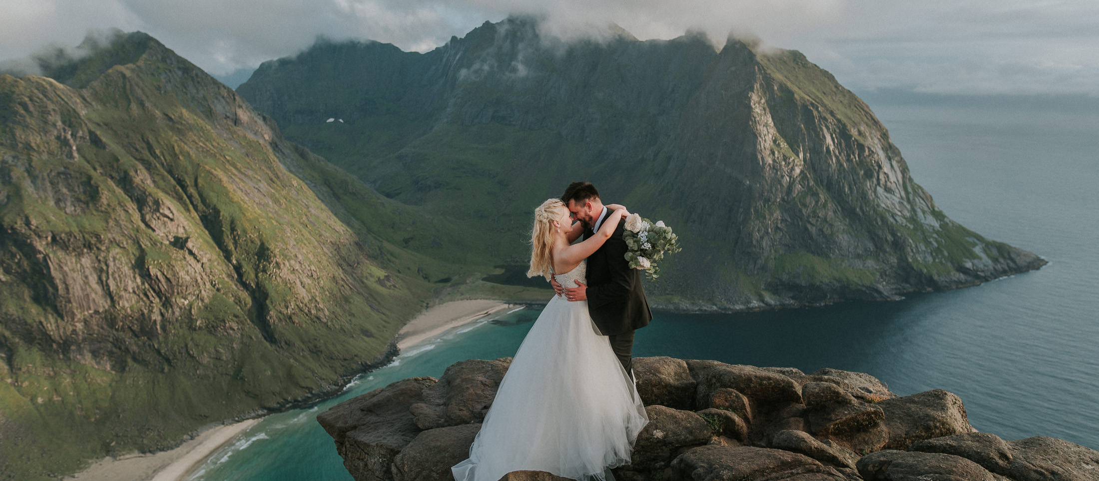 Bride and groom enjoying their adventure wedding in Lofoten - standing on the mountaintop with an epic scenery in the background