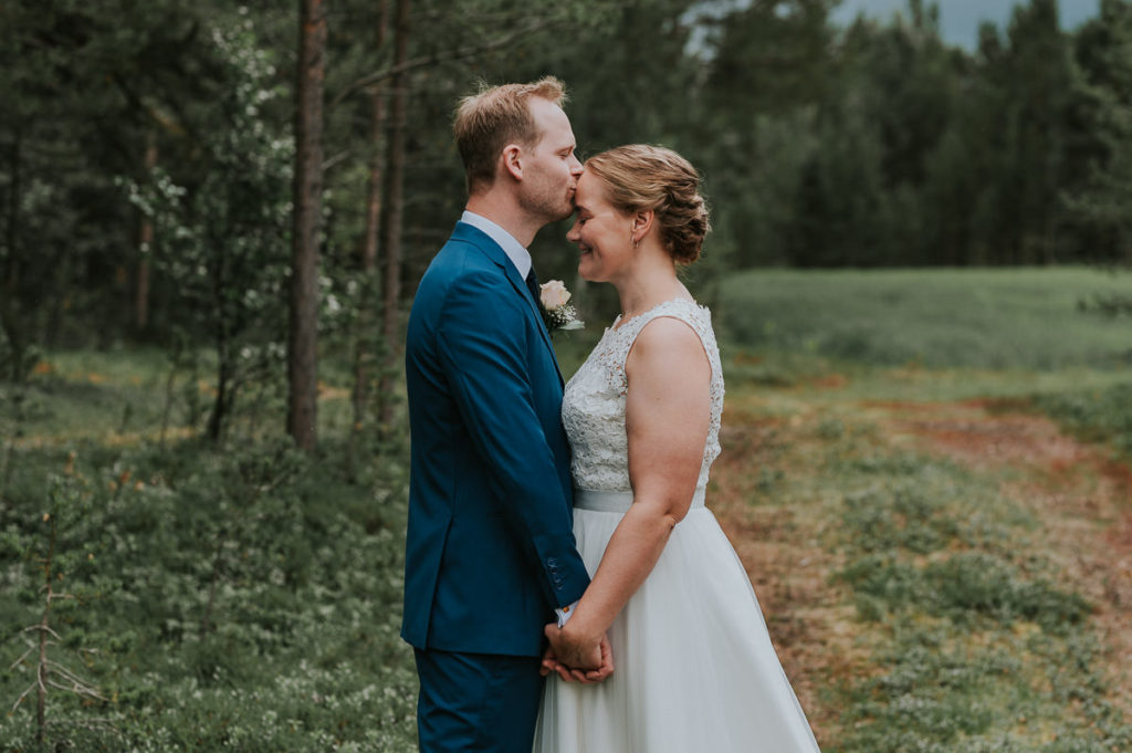Brudgommen kysser sin brud på panna i fine omgivelser i en skog i Alta