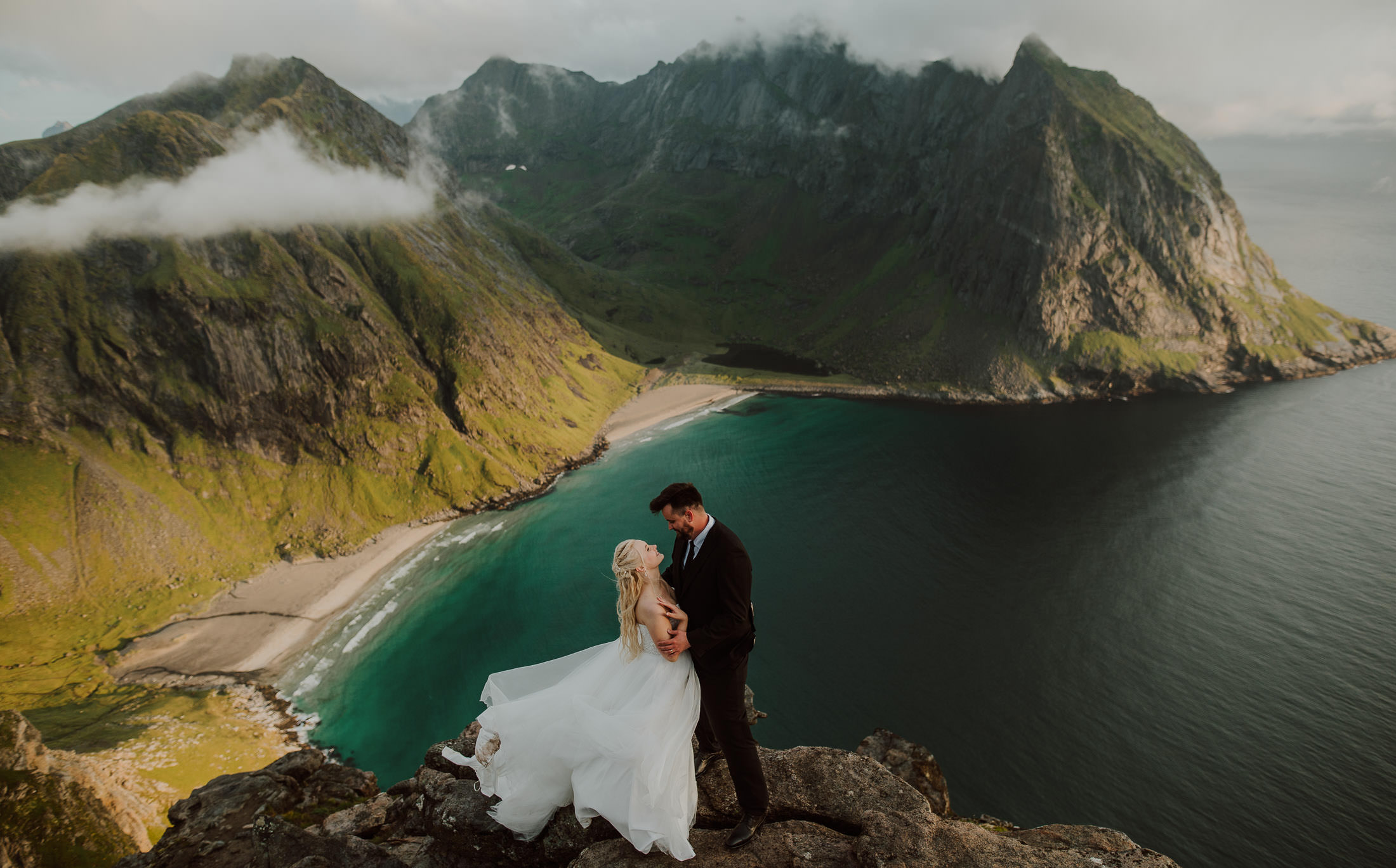 Bride and groom hugging each other on a breathtaking mountaintop in Lofoten Norway on the day of their elopement