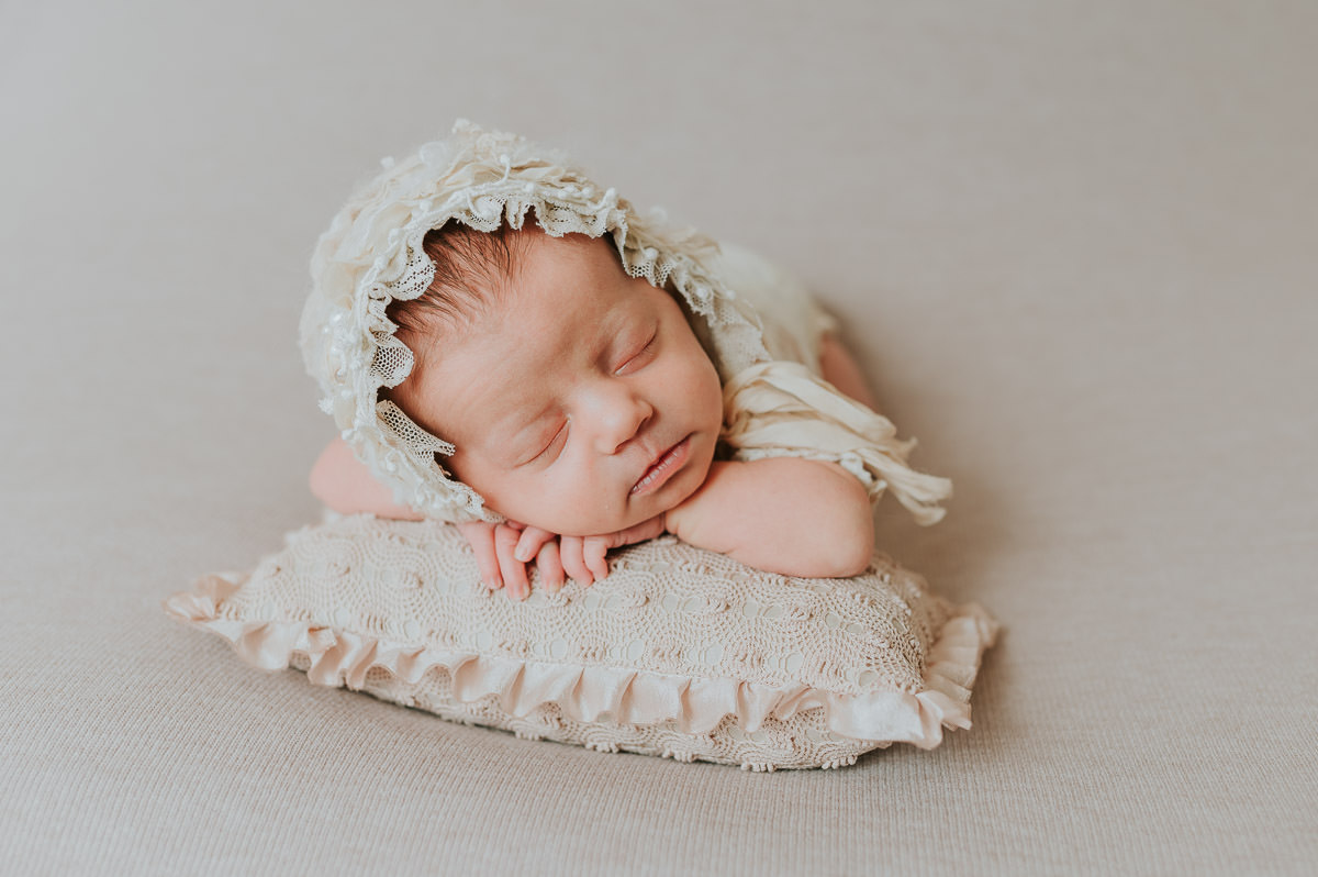 Nyfødt jente sover på en liten pute på beige fotobakgrunn på nyfødtfotografering i Alta hos TS Foto Design