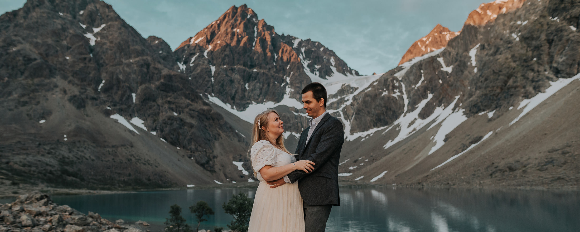 Pre-wedding in Norway in Lyngen Alps - bride and groom kissing in front of glacial lake and mountains