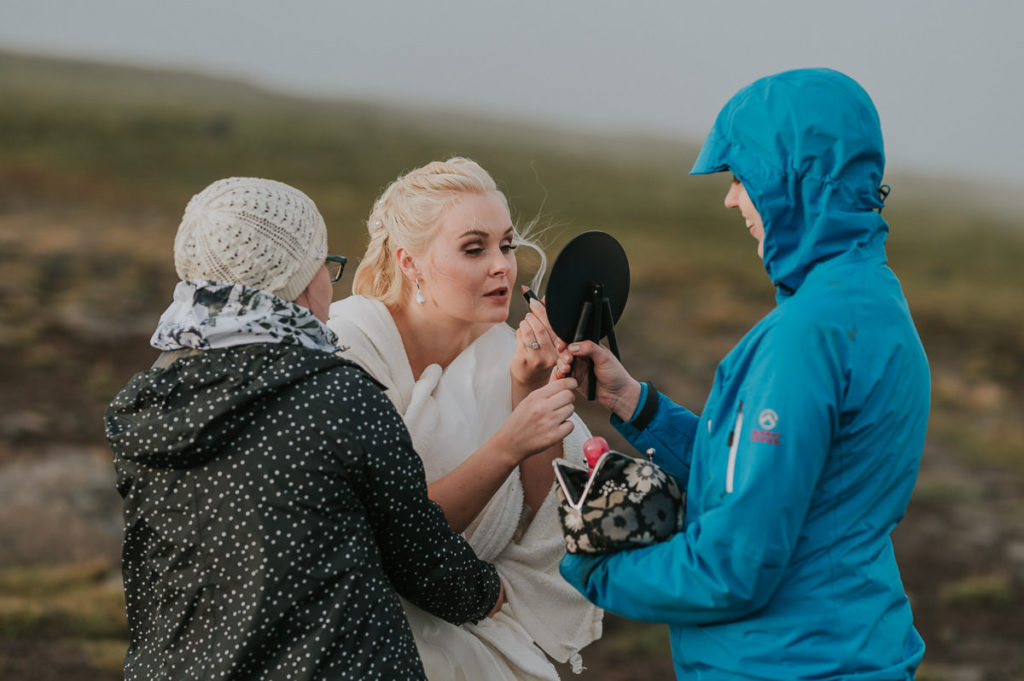 Bride and groom getting ready for their adventure wedding in Lofoten on a mountaintop while bridesmaids are helping up with the wedding attire