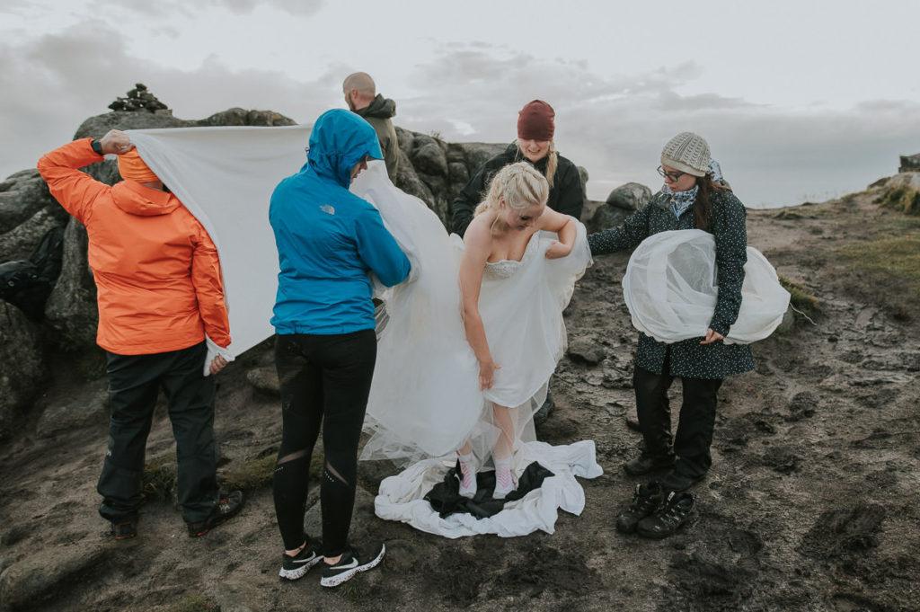 Bride and groom getting ready for their adventure wedding in Lofoten on a mountaintop while bridesmaids and groomsmen are helping up with the wedding attire