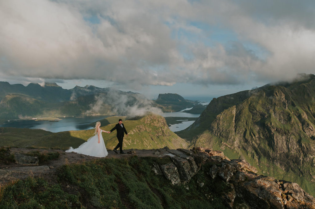 Bride and groom hiking in the mountains of Lofoten wearing their wedding attire and celebrating their adventure elopement wedding 