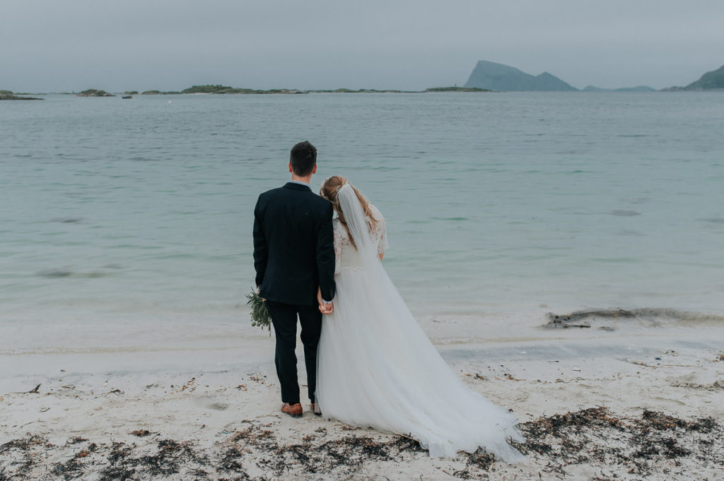 Bride and groom on a beach holding hands and looking at the beautiful view  - captured by Tromsø wedding photographer TS Foto Design