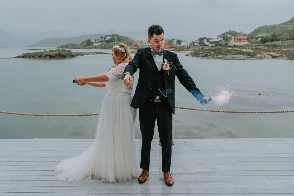 Bride and groom struggling to fire up smoke bombs while having funny expressions on their faces