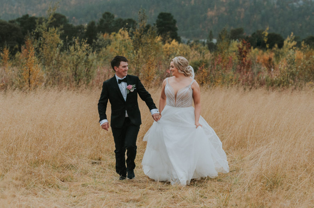 Brudeparfotografering i en nydelig gull stråfelt i Alta. Bryllupsfotografering på en flott senhøst dag. Bruden og brudgommen holder hendene og løper 