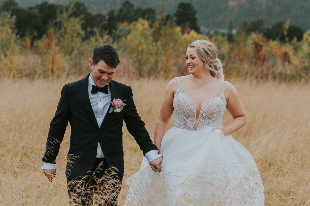 Bryllupsfotografering i en nydelig gull stråfelt i Alta. Bruden og brudgommen holder hendene og løper 