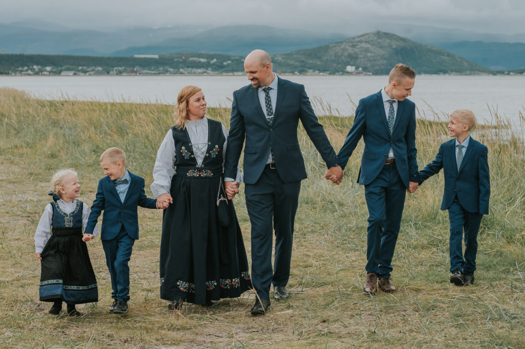 Konfirmantfotografering sammen med storfamilie i Alta. Alle familiemedlemmer er kledd i bunader og dress og spaserer langs sjøen 