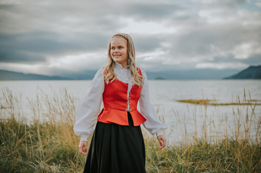 Portrett av en jente i finnmarksbunad ved siden av havet blant fine høstfarger  - på konfirmantfoto i Alta