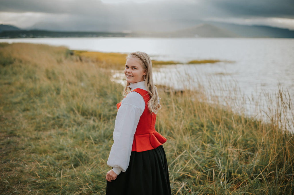 Portrett av en jente i finnmarksbunad ved siden av havet blant fine høstfarger  - på konfirmantfoto i Alta
