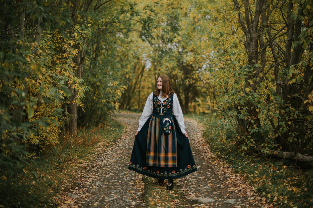 Portrett av ei jente i nordlandsbunad foran høstkledd skog på konfirmantfotografering i Alta