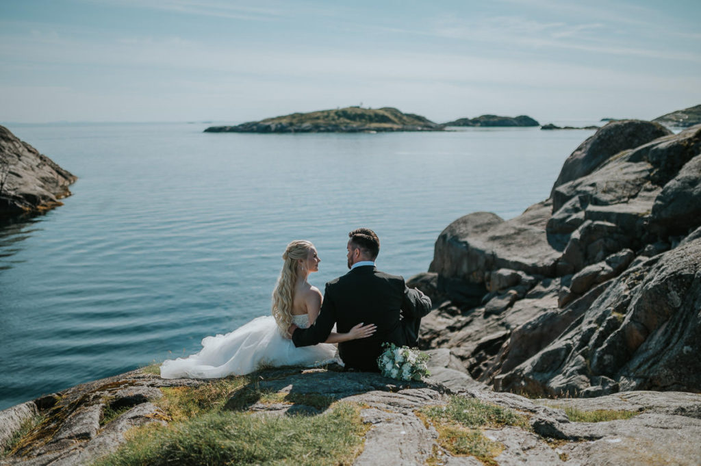 Bridal couple enjoying a sunny and warm summer day while watching the sea and mountains in Lofoten on the day of their wedding in Nyvågar Kabelvåg
