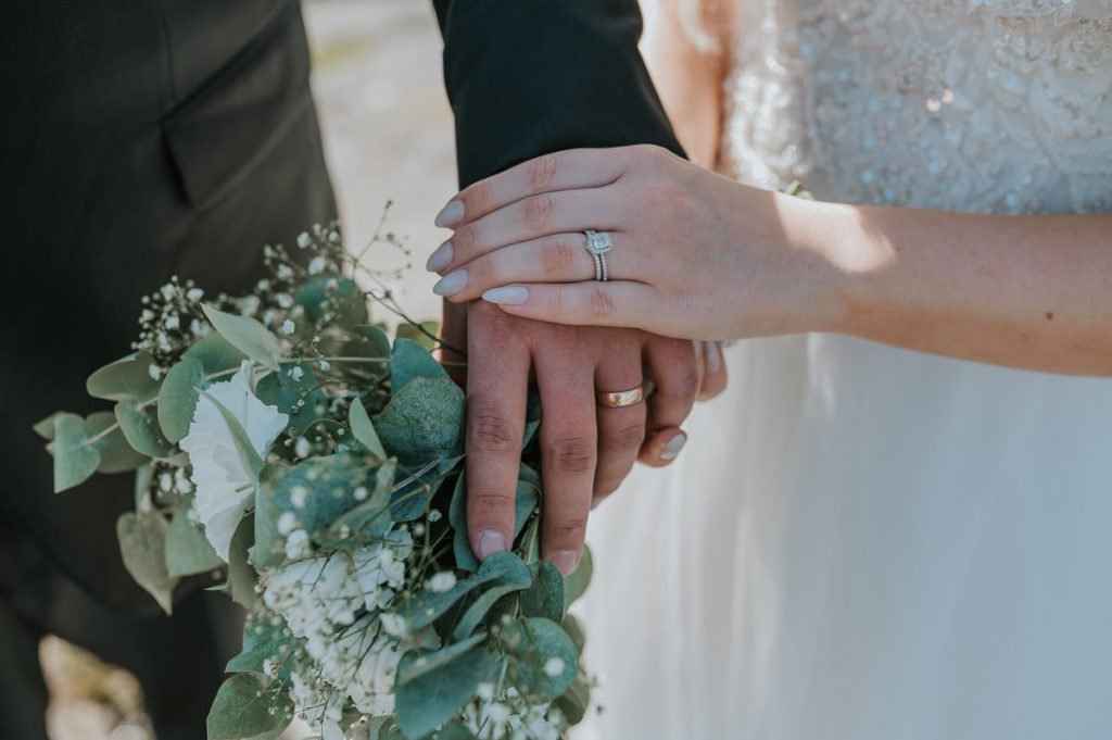 Bride and groom showing their wedding rings and a bouquet in white color