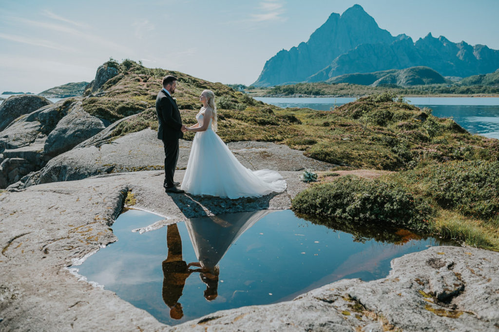 Bridal portrait in Lofoten Norway where bride and groom are looking at each other and their reflection is mirrored in a lake nearby