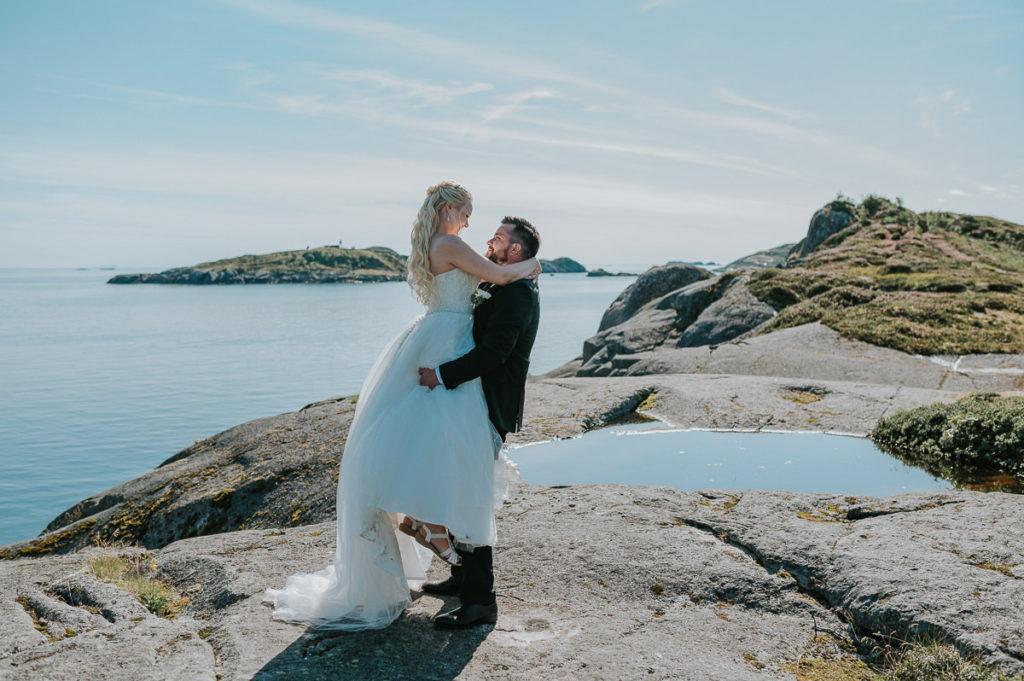 Bridal couple enjoying a sunny and warm summer day while watching the sea and mountains in Lofoten on the day of their wedding in Nyvågar Kabelvåg