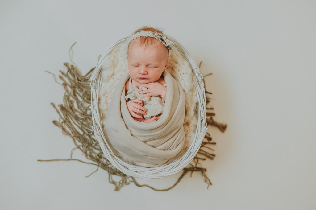 Nyfødt jente i en hvit kurv på en beige fotobakgrunn på nyfødtfotografering i Alta
