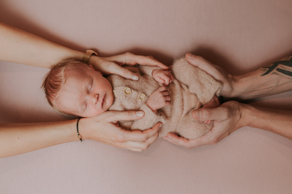 Baby jente med rosa klær  ligger i hendene til sine foreldre og sover 