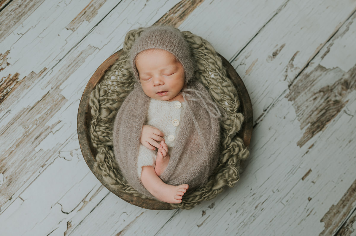 Nyfødtfotografering med en baby gutt som ligger i en trebolle på beige bakgrunn i fotostudio i Alta