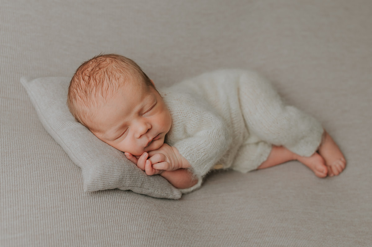 Nyfødt gutt sover på en liten pute på beige fotobakgrunn på nyfødtfotografering i Alta hos TS Foto Design