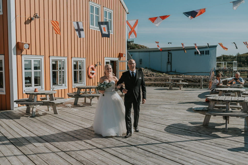 A bride and her father walking down the aisle outdoors at Nyvågar rorbuhotell in Lofoten during wedding ceremony