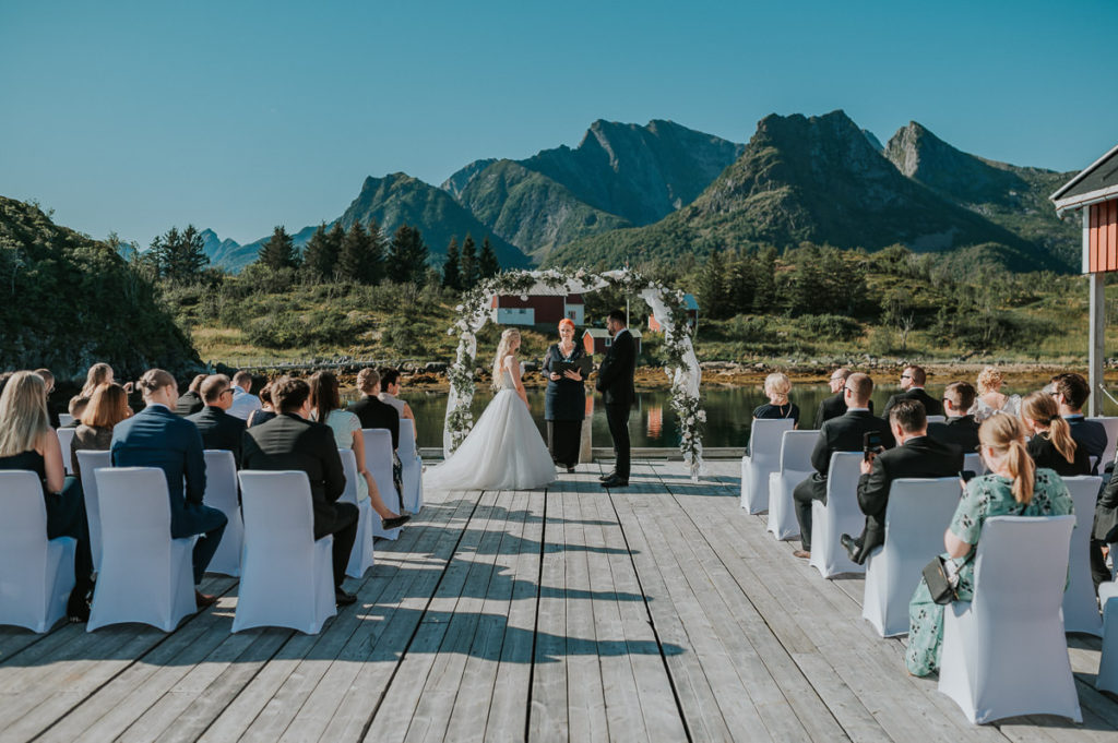 Outdoor wedding ceremony on a pier at Nyvågar rorbu hotell in Lofoten. Bride and groom are having a civil ceremony performed by a mayor 