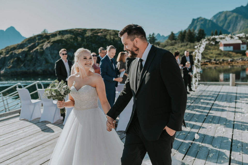 Bride and groom walking hand in hand after their outdoor adventure wedding ceremony in Lofoten, Norway. The guests are throwing flower petals on them and everybody is cheering