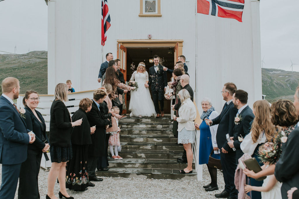 Bride and groom walking out of Hillesøy church after their wedding ceremony. The guests are throwing fresh flower petal confetti at them - captured by Tromsø wedding photographer TS Foto Design