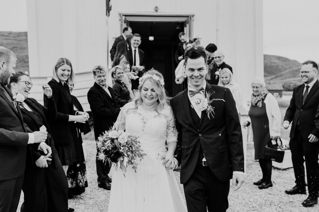 Bride and groom walking out of Hillesøy church after their wedding ceremony. The guests are throwing fresh flower petal confetti at them and the couple is laughing - captured by Tromsø wedding photographer TS Foto Design