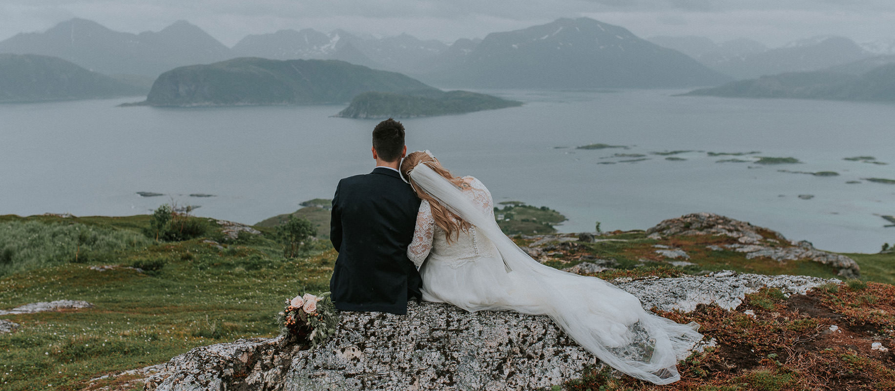 Bride and groom sitting on rocks on a mountaintop in Sommarøy - captured by Tromsø wedding photographer TS Foto Design